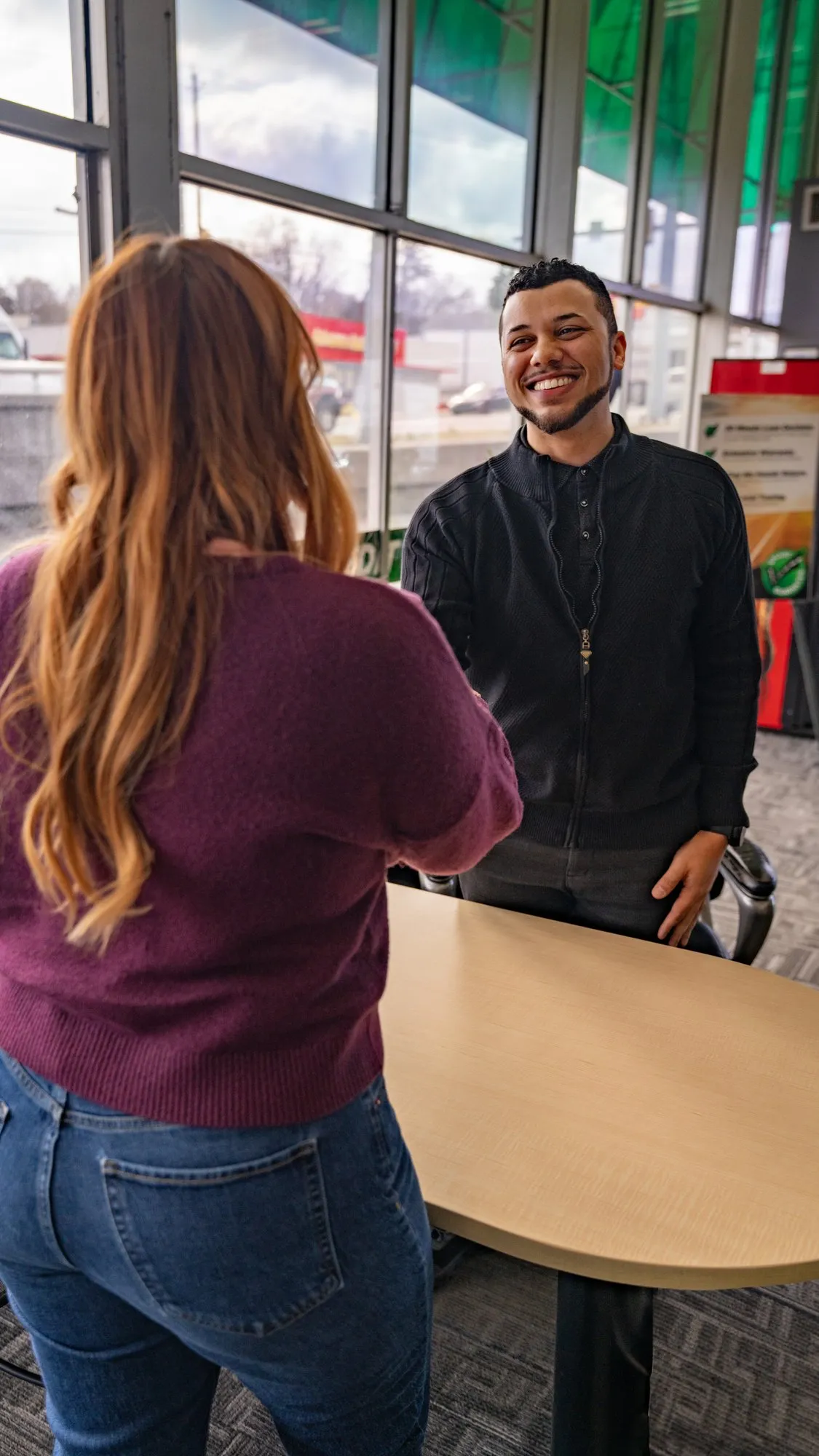 A Smart Auto salesperson smiling across a desk at a customer in the dealership showroom