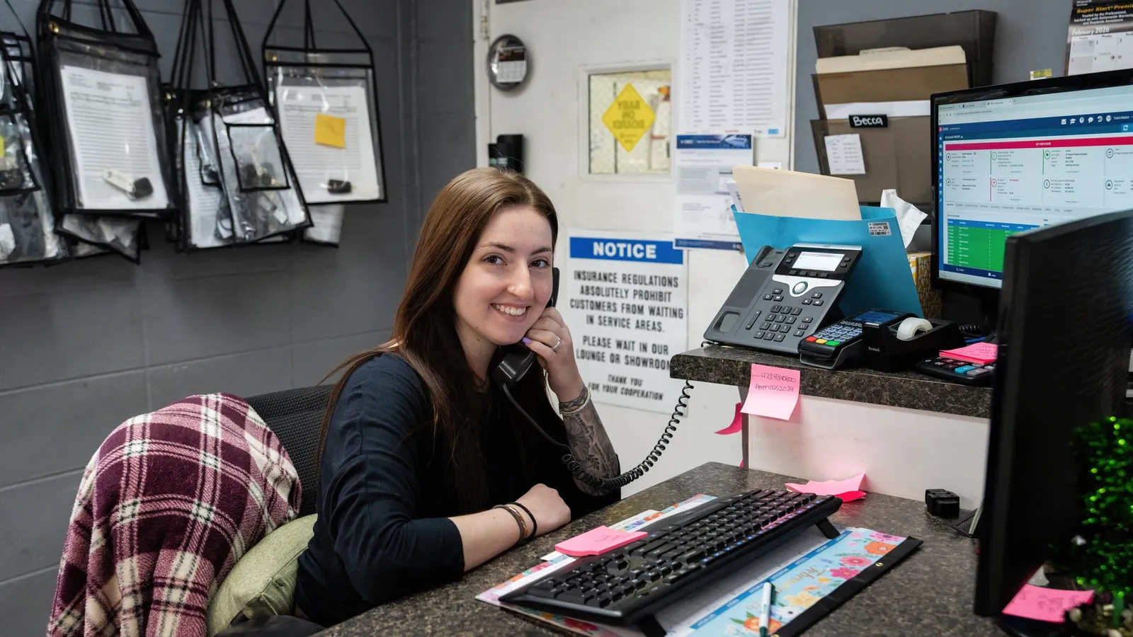 A Smart Auto service receptionist taking a call at her desk, dealership management software open on the monitor beside her